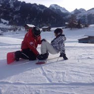 A snowboard instructor is helping a student to find balance on the snowboard during private snowboarding lessons for kids and adults with Swiss Ski School Zweisimmen.