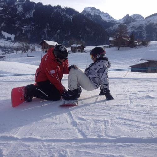 Lezioni private di snowboard - Saanenmöser e Schönried con Swiss Ski School Zweisimmen Un maestro di snowboard aiuta un allievo a trovare l'equilibrio sulla tavola durante le lezioni private di snowboard per bambini e adulti della Scuola Svizzera di Sci Zweisimmen.