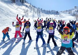 Kids are standing on a slope, their hands in the air, ready to start their Kids Ski Lessons (7-12 y.) for All Levels with the ski school ESF Isola 2000.