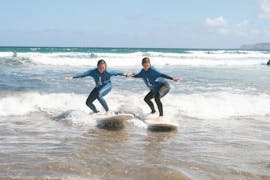 Dos participantes surfeando las olas durante una clase grupal en la playa de Famara con Surf&SUP School3s Lanzarote.
