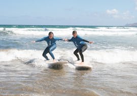 Two participants surfing the waves during a group lesson in Famara beach with Surf&SUP School3s Lanzarote. 