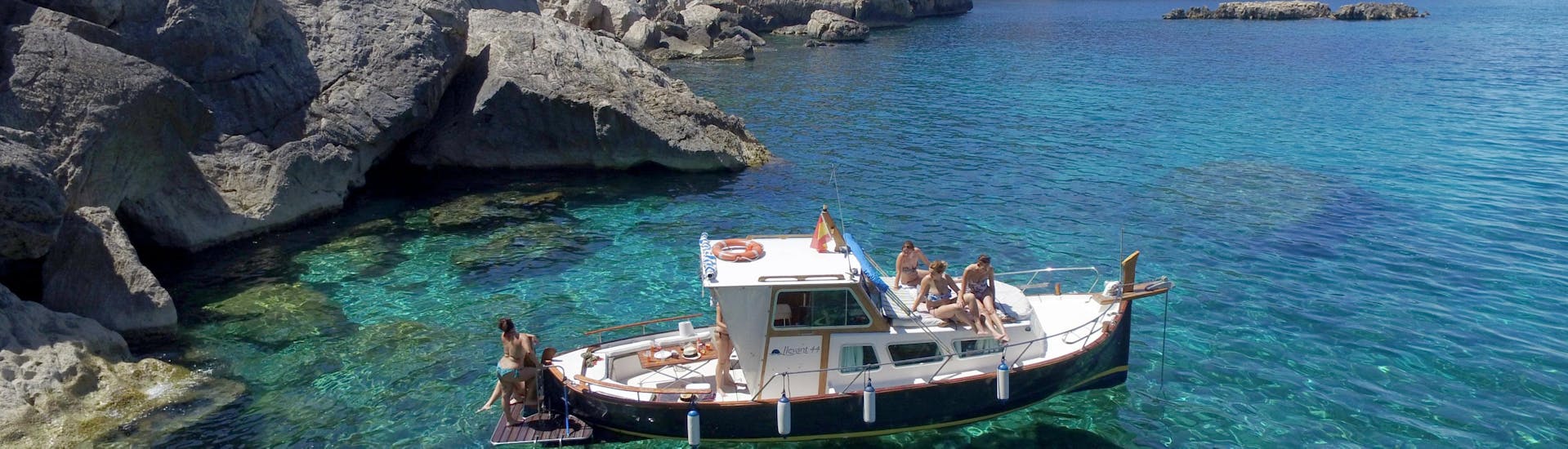 Una barca di Take Off Ibiza galleggia nelle acque cristalline durante il giro in barca privato lungo la costa di Ibiza da San Antonio.
