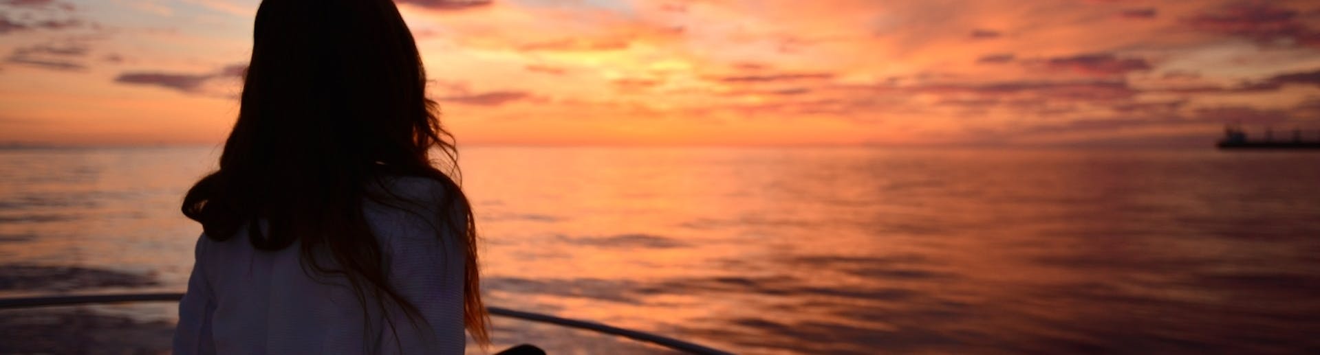 Eine Frau bewundert den Sonnenuntergang während einer privaten Bootsfahrt bei Sonnenuntergang entlang der Küste Ibizas mit Take Off Ibiza.