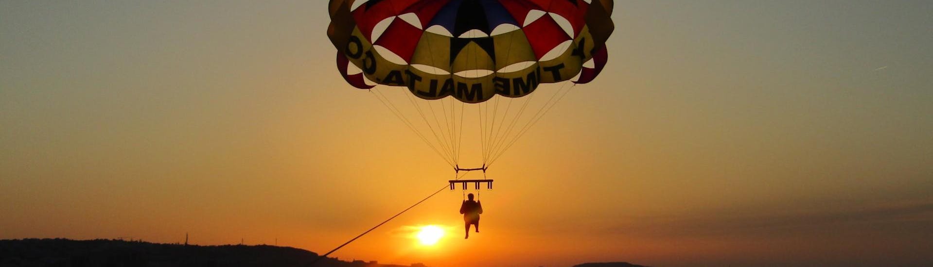 Un jeune homme vole au-dessus de la mer en profitant de la vue imprenable du coucher de soleil à Malte lors d'un vol en Parachute ascensionnel à St George's Bay avec Flytimemalta.