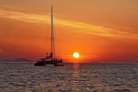 Catamaran sur l'eau, avec le coucher de soleil à l'arrière.
