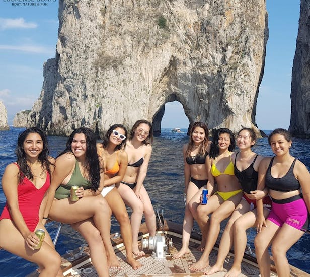 Un grupo de amigos posando detrás de las rocas Faraglioni durante el clásico viaje en barco de Sorrento a Capri, con Lubrense Boats Costiera Amalfitana.