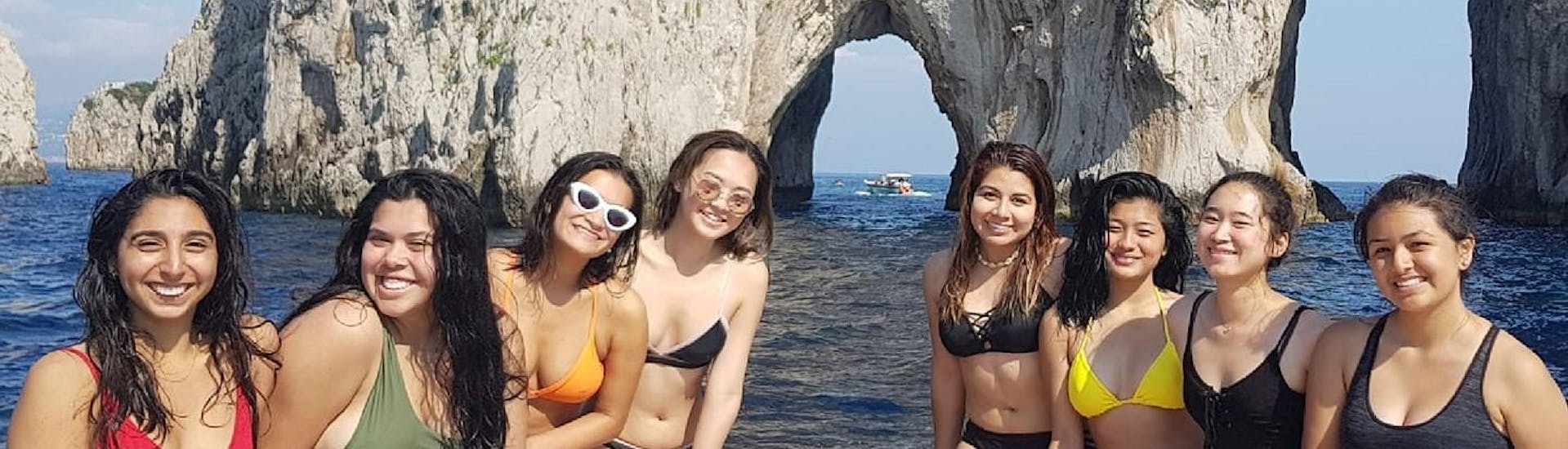 Groupe d'amis posant derrières les roches Faraglioni pendant une balade en bateau typique de Sorrente à Capri avec Lubrense Boats Costiera Amalfitana.