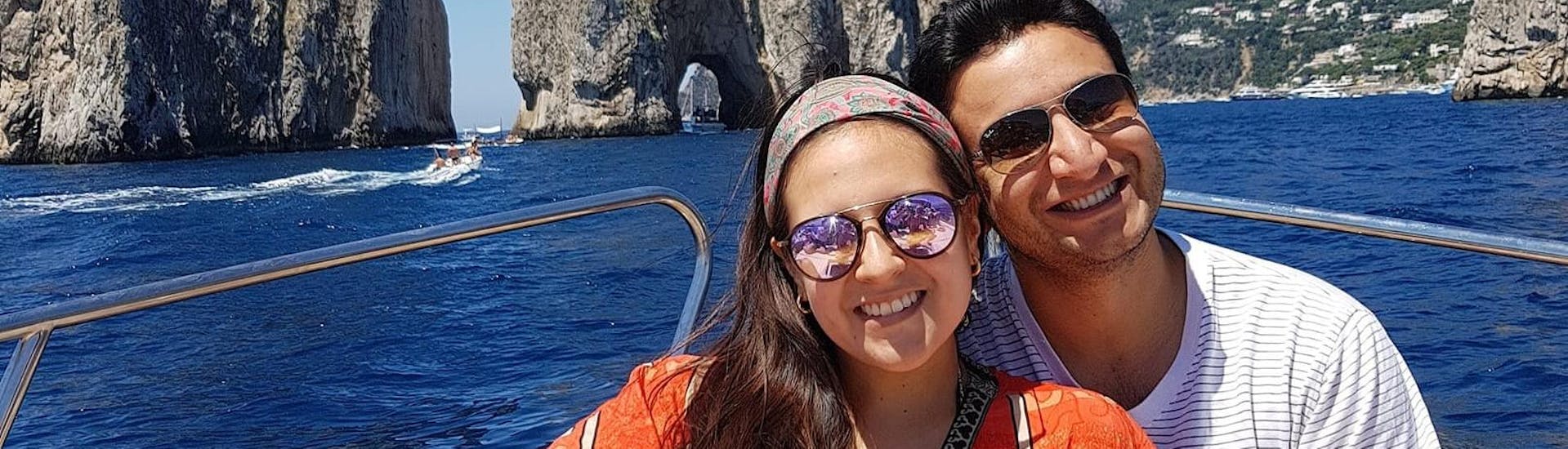 Una pareja feliz posando para una foto detrás de las rocas Faraglioni, durante el viaje en barco privado desde Positano a Capri, con Lubrense Boats Costiera Amalfitana.