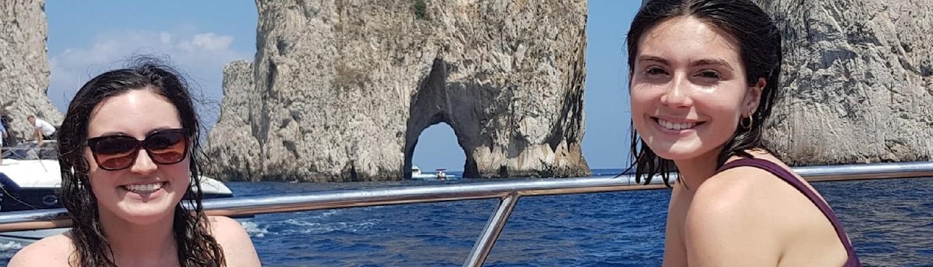 Dos amigos sonrientes posando frente a las rocas Faraglioni durante el viaje en barco privado desde Amalfi a Capri, con Lubrense Boats Costiera Amalfitana.