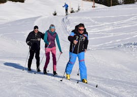 Una coppia si esercita nella tecnica classica dello sci di fondo insieme al proprio istruttore privato durante le lezioni private di sci di fondo per tutti i livelli della Scuola ABC Snow Sports di Arosa.