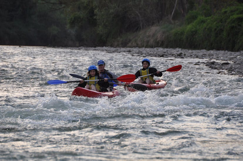Un padre y sus dos hijos reman intensamente durante el Kayak en el río Adige en la Terra dei Forti con Pescantina Rafting Bussolengo.