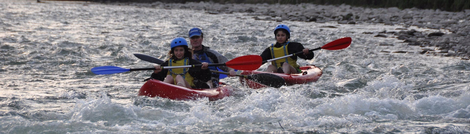 Un padre y sus dos hijos reman intensamente durante el Kayak en el río Adige en la Terra dei Forti con Pescantina Rafting Bussolengo.