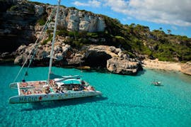 De boot van Magic Catamarans ligt voor anker op het strand van Es Trenc terwijl passagiers een duik nemen in het blauwe mediterrane water.