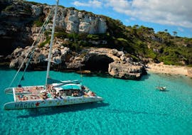 Das Boot von Magic Catamarans liegt am Strand von Es Trenc vor Anker, während die Passagiere ein Bad im blauen Mittelmeerwasser nehmen.