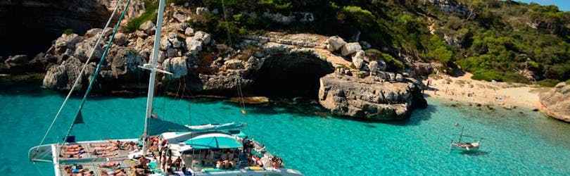 La barca di Magic Catamarans è ancorata alla spiaggia di Es Trenc mentre i passeggeri fanno il bagno nelle acque blu del Mediterraneo.