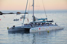 Een boot van Magic Catamarans vaart rond de baai van Roses terwijl de zon ondergaat tijdens deze catamarantocht bij zonsondergang.