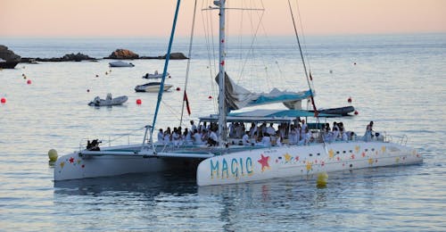 Balade en catamaran au coucher du soleil depuis Roses avec Magic Catamarans Mallorca Un bateau de Magic Catamarans navigue autour de la baie de Roses alors que le soleil se couche dans cette Sortie en catamaran au coucher du soleil depuis Roses.