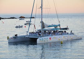A boat from Magic Catamarans is sailing around the bay of Roses while the sun is setting in this sunset catamaran tour.