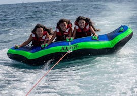 Three women are on top of the Crazy Boat of Sea Riders Badalona while being towed by a boat in Barcelona Bay.