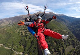 Dos personas saludan a la camara mientras hacen parapente en un vuelo biplaza a gran altura con Parapente Pirineos en en Valle de Arán.