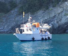 Durante el viaje en barco por Cinque Terre con barbacoa de pescado, se puede ver el barco de Aquamarina Cinque Terre pasando por delante de una antigua iglesia.