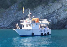 Durante el viaje en barco por Cinque Terre con barbacoa de pescado, se puede ver el barco de Aquamarina Cinque Terre pasando por delante de una antigua iglesia.