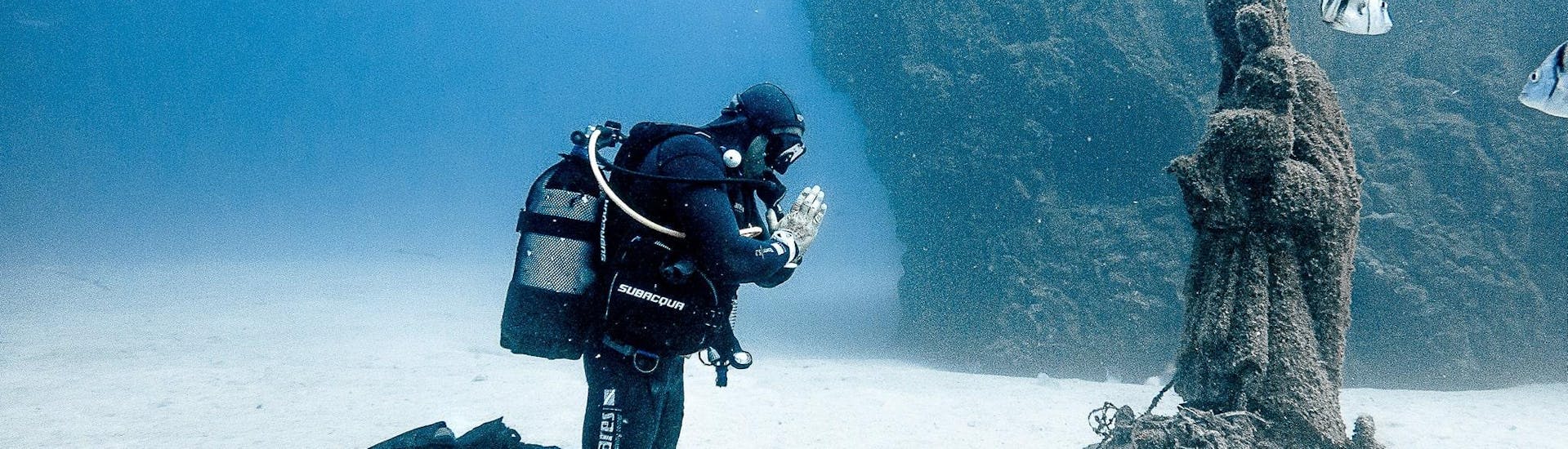 A diver kneels in front of a statue at the bottom of the sea at Los Cristianos beach with Diving Atlantis. 