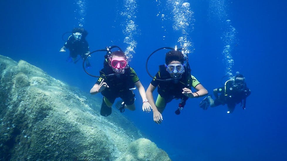 Un groupe de plongeurs sourit sous l'eau pour la photo pendant le cours PADI Open Water Diver à Baie de Calvi pour débutants avec Calvi Plongée.