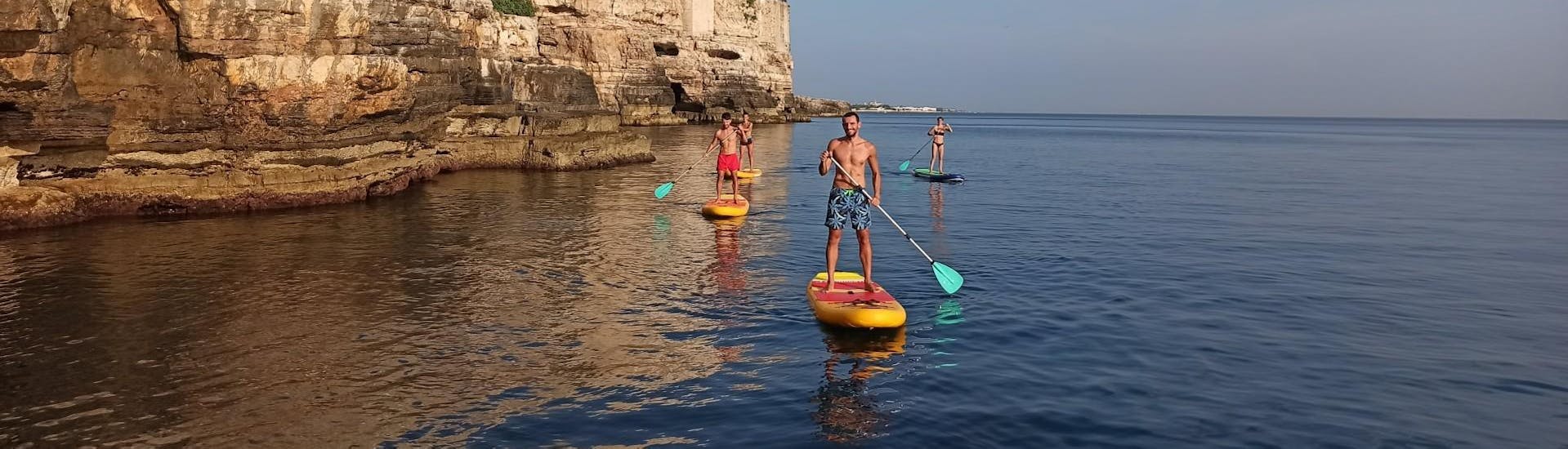 Eine Gruppe von Freunden hat Spaß bei der Stand Up Paddle Tour zu den Höhlen von Polignano a Mare.