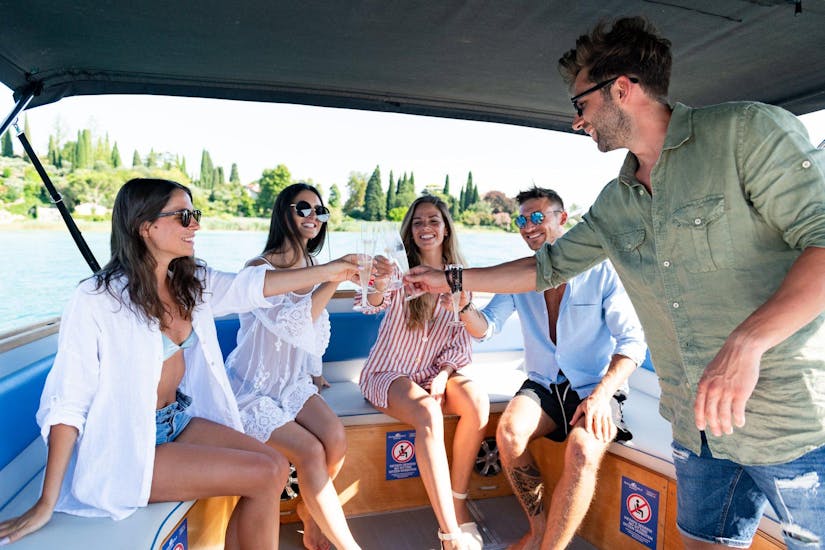 Un grupo de amigos levanta una copa de vino a bordo de una lancha de Sirmione Boats durante un viaje en barco a los Castillos del Lago de Garda y Bardolino.
