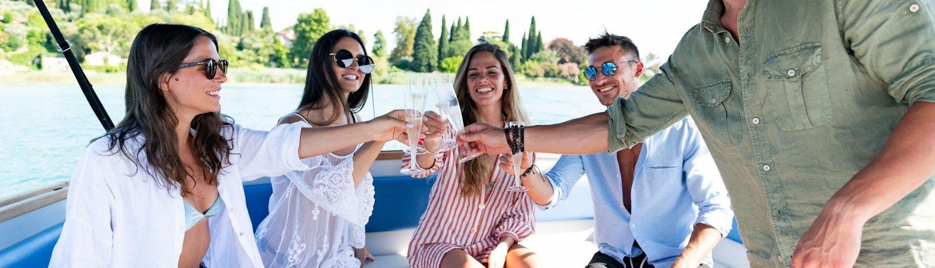 Un gruppo di amici brinda con un calice di vino a bordo di un motoscafo di Sirmione Boats durante un Giro in barca ai Castelli del Lago di Garda e Bardolino.