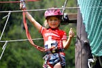 Een jong meisje dat plezier heeft tijdens het touwenparkour in het avonturenpark bij de Noce River met Extreme Waves.