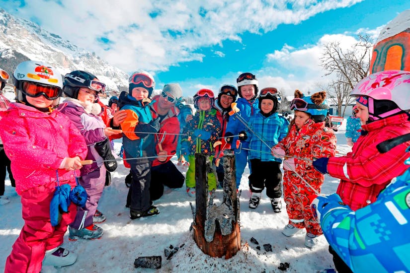 Een groep kinderen roostert appels tijdens hun skilessen voor kinderen voor beginners bij skischool Ramsau.