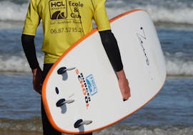 A man has a surfboard while looking at the sea during Surfing Lessons on Lacanau Beach with HCL Lacanau Surf School