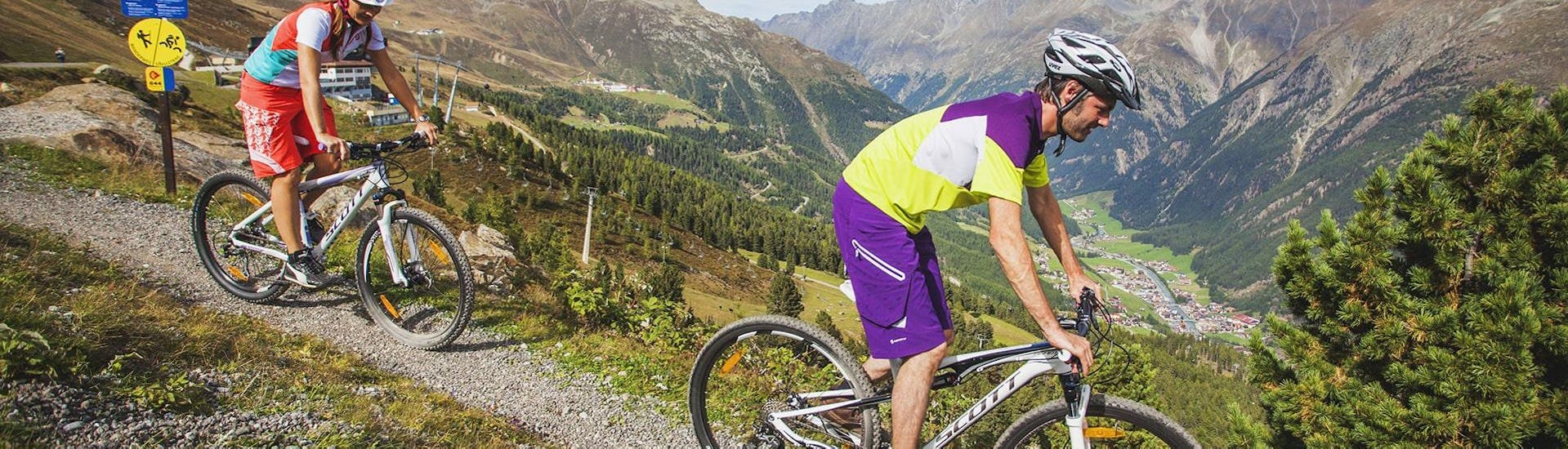 Zwei Männer fahren mit ihren Fahrrädern, die sie beim Radverleih Skischule & Bikeverleih AGE Ötz-Hochötz im Ötztal ausgeliehen haben, einen Bergweg entlang.