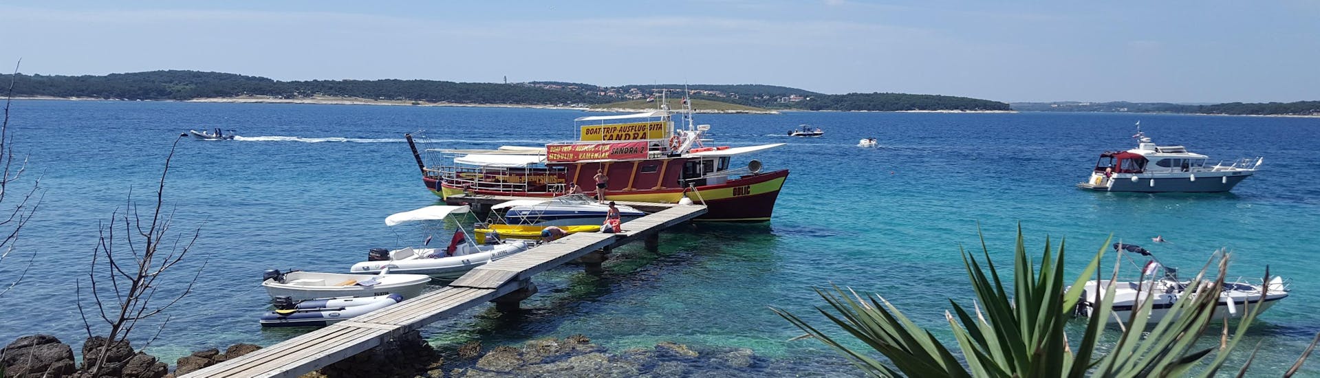 Le bateau de Medulin Excursions est amarré à l'embarcadère alors que les gens montent à bord pour la balade en bateau au Cap Kamenjak depuis Medulin avec baignade.