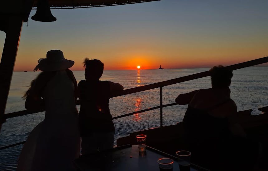 Menschen beobachten den Sonnenuntergang während der Bootstour zur Delfinbeobachtung bei Sonnenuntergang in Richtung Horizont.