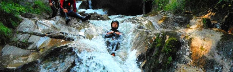A man from the Sporterlebnis Camp Pristavec Obervellach slides down a waterfall while canyoning.