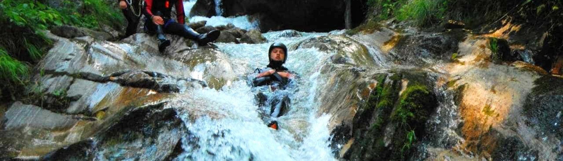 Een man van de Sporterlebnis Camp Pristavec Obervellach glijdt tijdens het canyoning van een waterval.