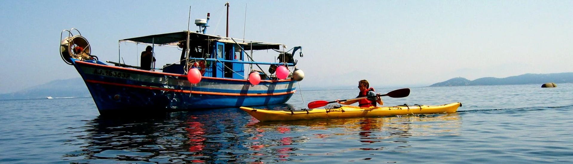 Un homme qui a loué un kayak de mer dans le golfe de Porticcio avec Cors'Aventure salut un bâteau de pêche.