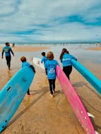 Four kids are carying their surf board and following their instructor during a surf lesson on Matosinhos Beach near Porto with Fish Surf School.