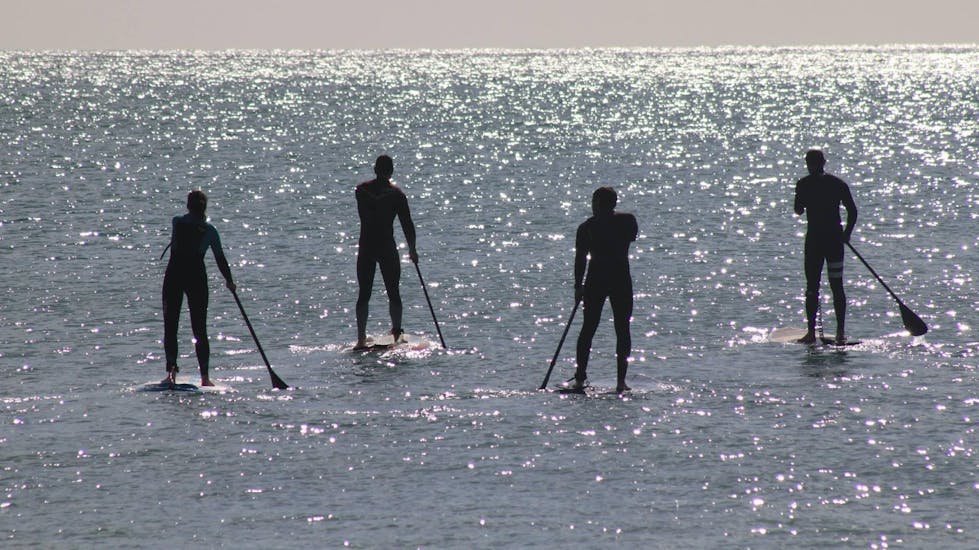 Four people on sup-boards from Nauticdrive in the Atlantic Ocean in front of Praia da Rocha Baixinha.