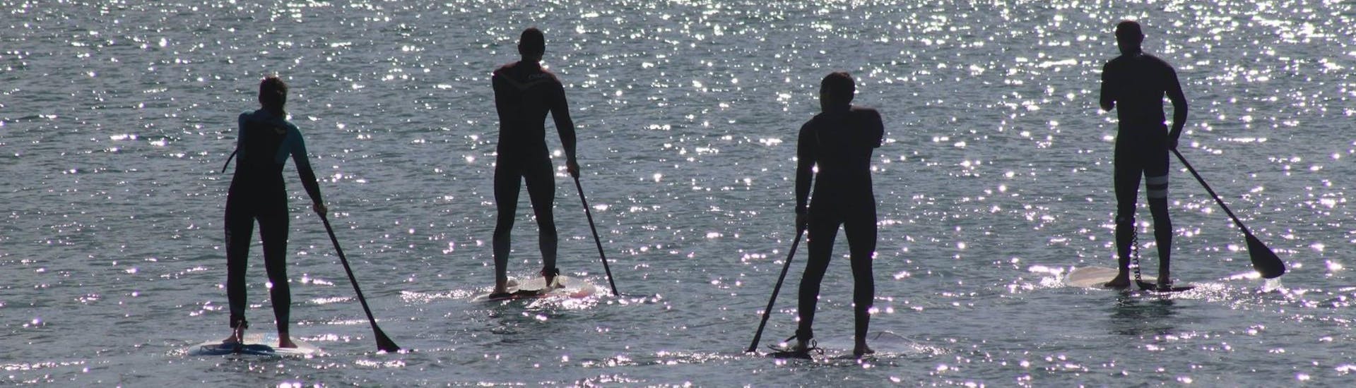 Vier Leute auf Sup-boards von Nauticdrive im Atlantischen Ozean vor dem Strand Praia da Rocha Baixinha. 