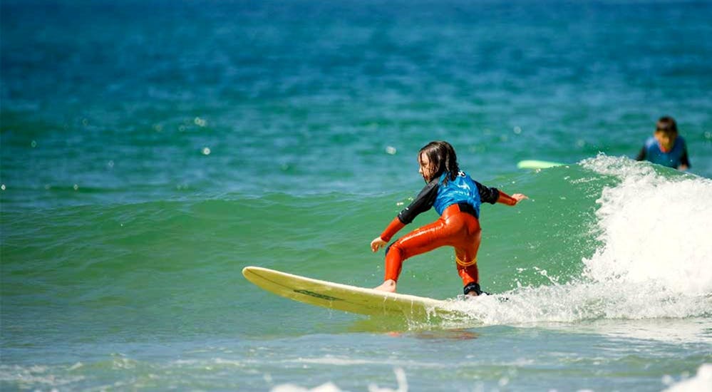 Un petit garçon prend une vague durant un cours de surf pour enfant sur la plage du Penon avec Surf Evolution Seignosse. 