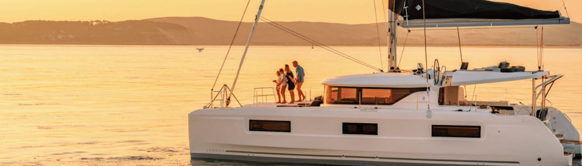 Photo of the catamaran at sunset used for the Premium Catamaran Tour to the Hot Springs with BBQ at sunset with Spiridakos Sailing Cruises Santorini.
