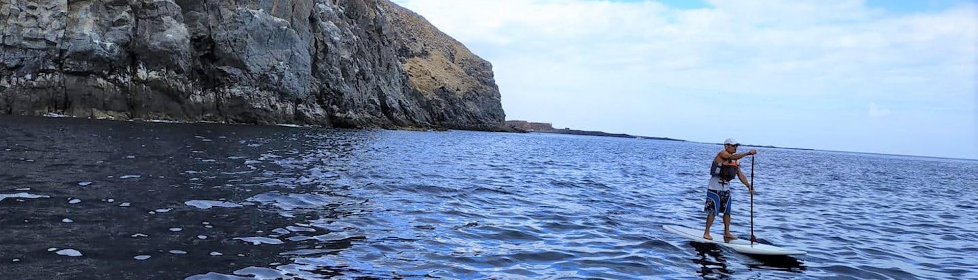 Un hombre se monta en un SUP cerca de la playa de Los Cristianos con Kayak Academy Tenerife. 