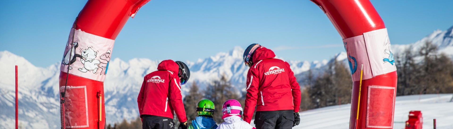 Deux moniteurs de l'ESS Veyzonnaz aident des jeunes enfants à faire leurs premiers pas à ski lors d'un cours particulier de ski pour enfants de 2 ans et demi à 5 ans.