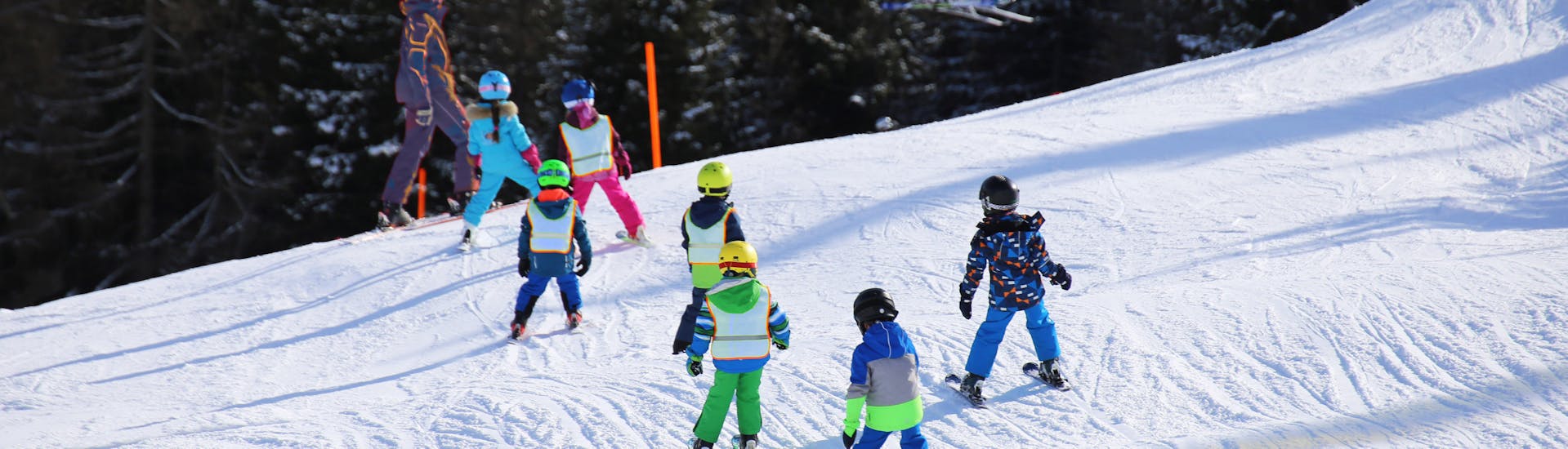 A group of young skiers is following their ski instructor from Family Ski School GO! Bad Gastein on the slope during the Kids Ski Lessons (7-11 y.) for First Timers.