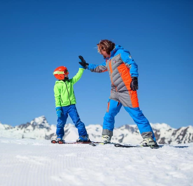 Geweldige foto van een ski-instructeur en een kind die elkaar een high-five geven in Limone tijdens een van de kinderskilessen (vanaf 6 jaar oud) voor beginners.