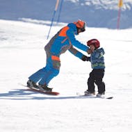 Moniteur de snowboard aidant un enfant à Limone pendant l'une des leçons privées de snowboard pour enfants de tous niveaux.